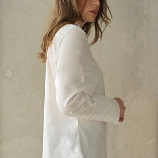 White button up shirt with a curved hem and wide collar, with three buttons  at the neck. Side view.