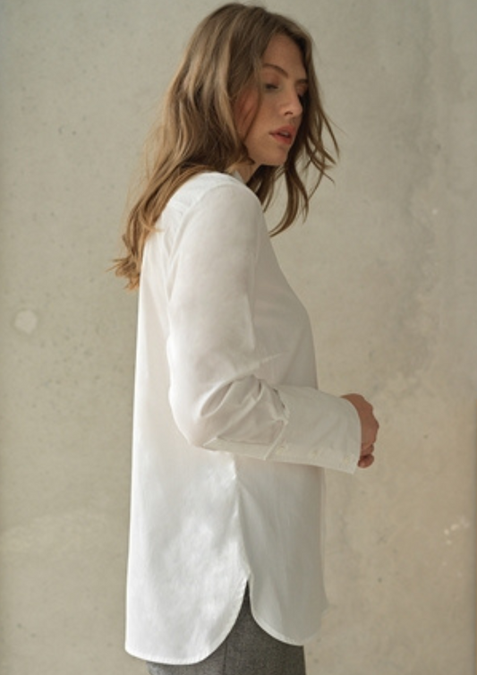 White button up shirt with a curved hem and wide collar, with three buttons  at the neck. Side view.