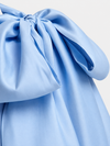 A close-up of a light blue satin-like fabric with a large gathered bow or tie detail, showing soft folds and sheen against a plain light background.