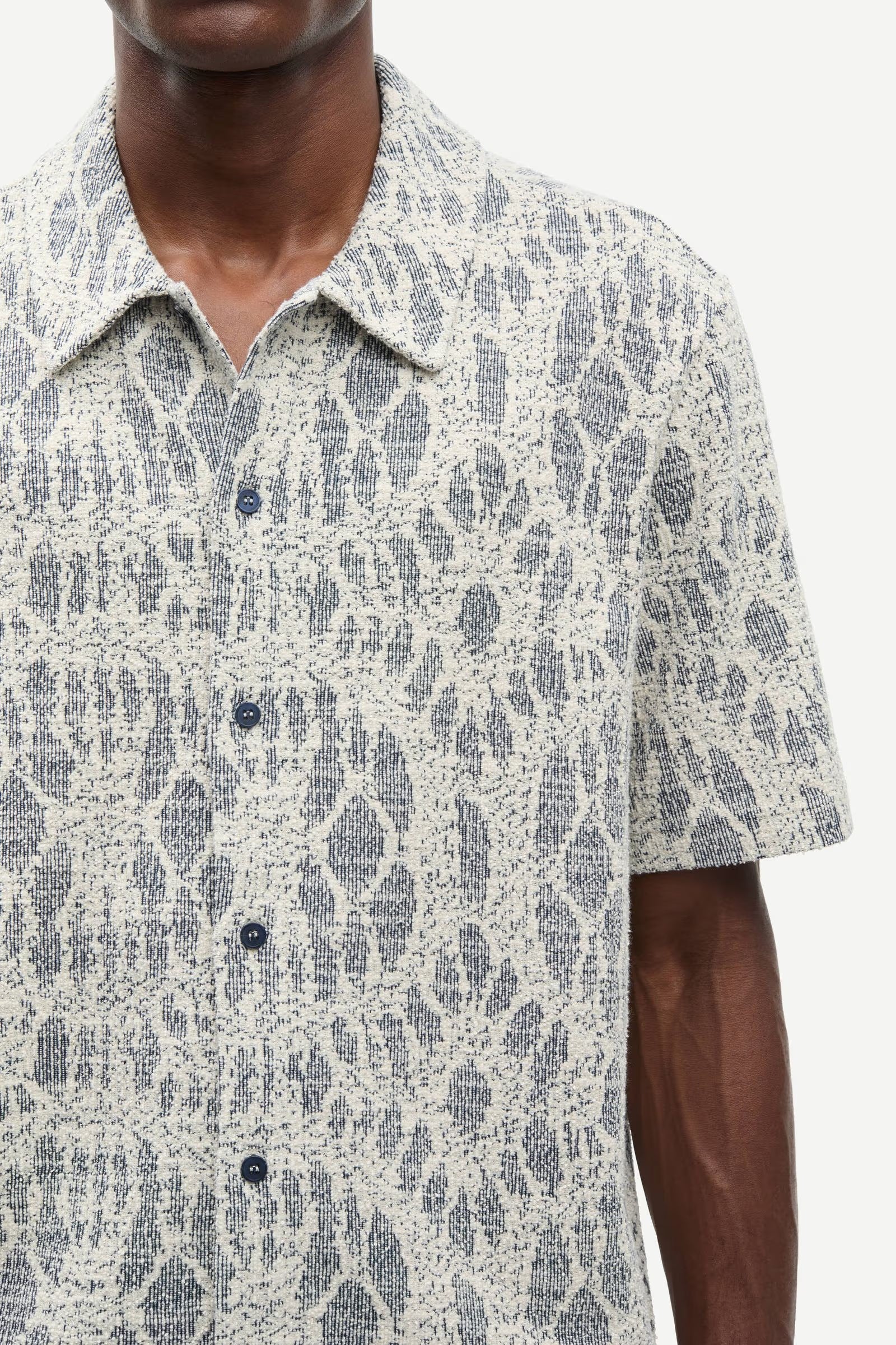 Man wearing a patterned shirt by samsoe samsoe with a neutral background