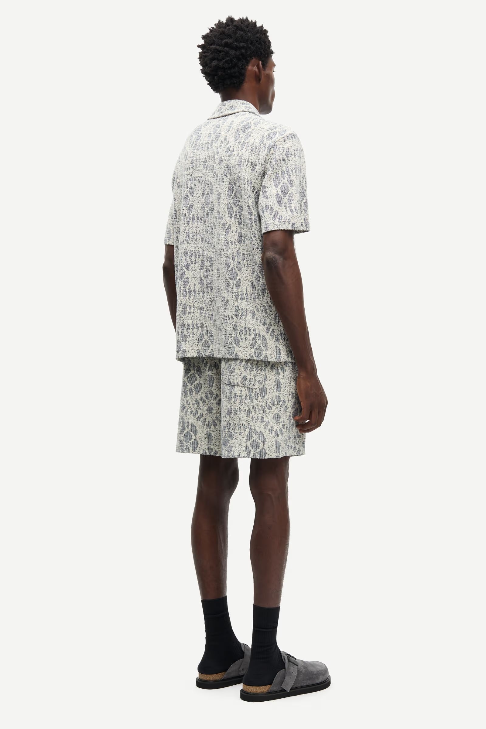 Man wearing a patterned shirt and shorts set by samsoe samsoe on a white background rear view