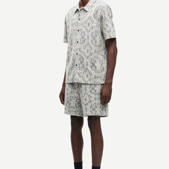 Man wearing a patterned shirt and shorts set by samsoe samsoe on a white background side view