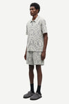 Man wearing a patterned shirt and shorts set by samsoe samsoe on a white background side view
