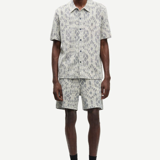Man wearing a patterned shirt and shorts set by samsoe samsoe on a white background