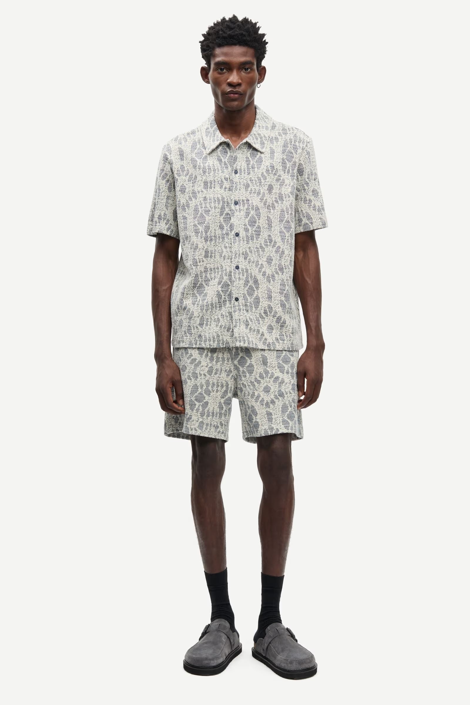 Man wearing a patterned shirt and shorts set by samsoe samsoe on a white background