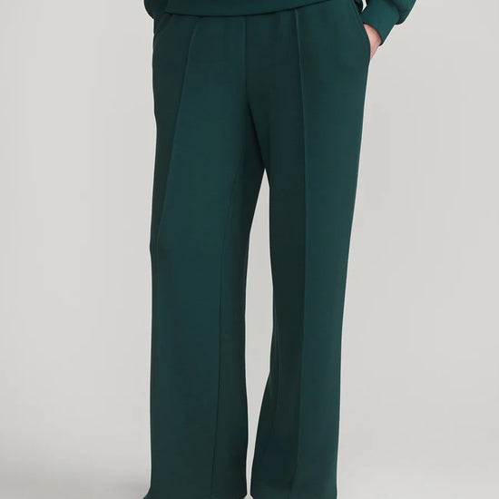 A person wearing dark teal wide-leg trousers and a matching dark teal sweatshirt, shown from the waist down against a light gray studio background.