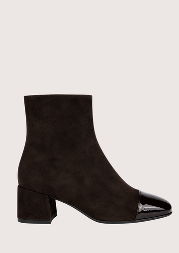 A pair of dark brown suede ankle boots with glossy patent leather cap toes and low block heels, shown against a light beige background.
