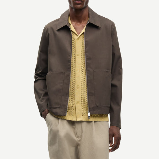 Man wearing a brown jacket by Samsoe Samsoe over a yellow shirt with beige pants on a white background