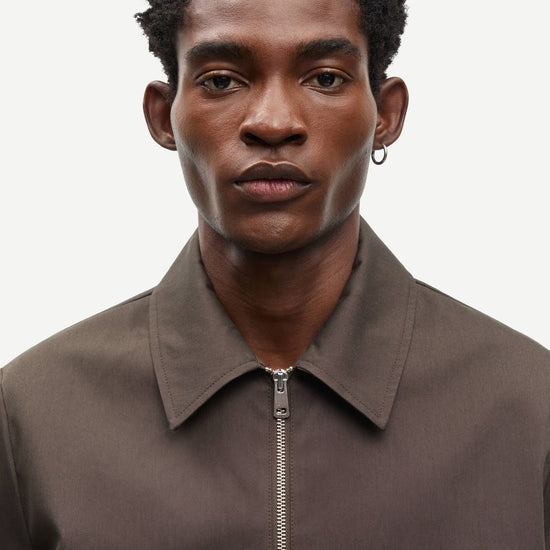 Man wearing a brown jacket by Samsoe Samsoe with a zipper on a white background