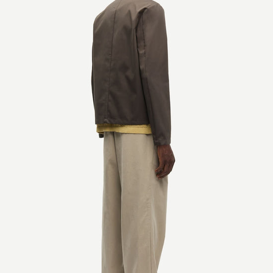 Man wearing a brown jacket by Samsoe Samsoe over a yellow shirt with beige pants on a white background rear view