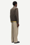 Man wearing a brown jacket by Samsoe Samsoe over a yellow shirt with beige pants on a white background rear view