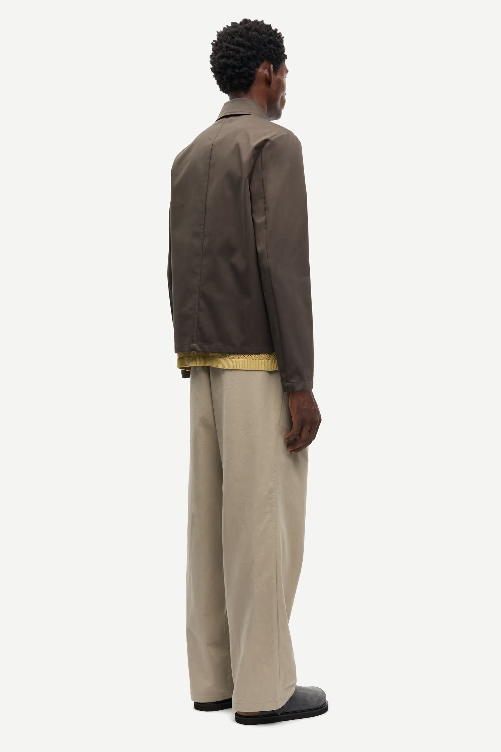 Man wearing a brown jacket by Samsoe Samsoe over a yellow shirt with beige pants on a white background rear view