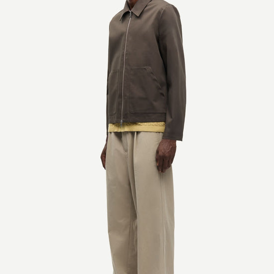 Man wearing a brown jacket by Samsoe Samsoe and beige pants on a white background side view