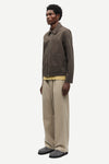 Man wearing a brown jacket by Samsoe Samsoe and beige pants on a white background side view