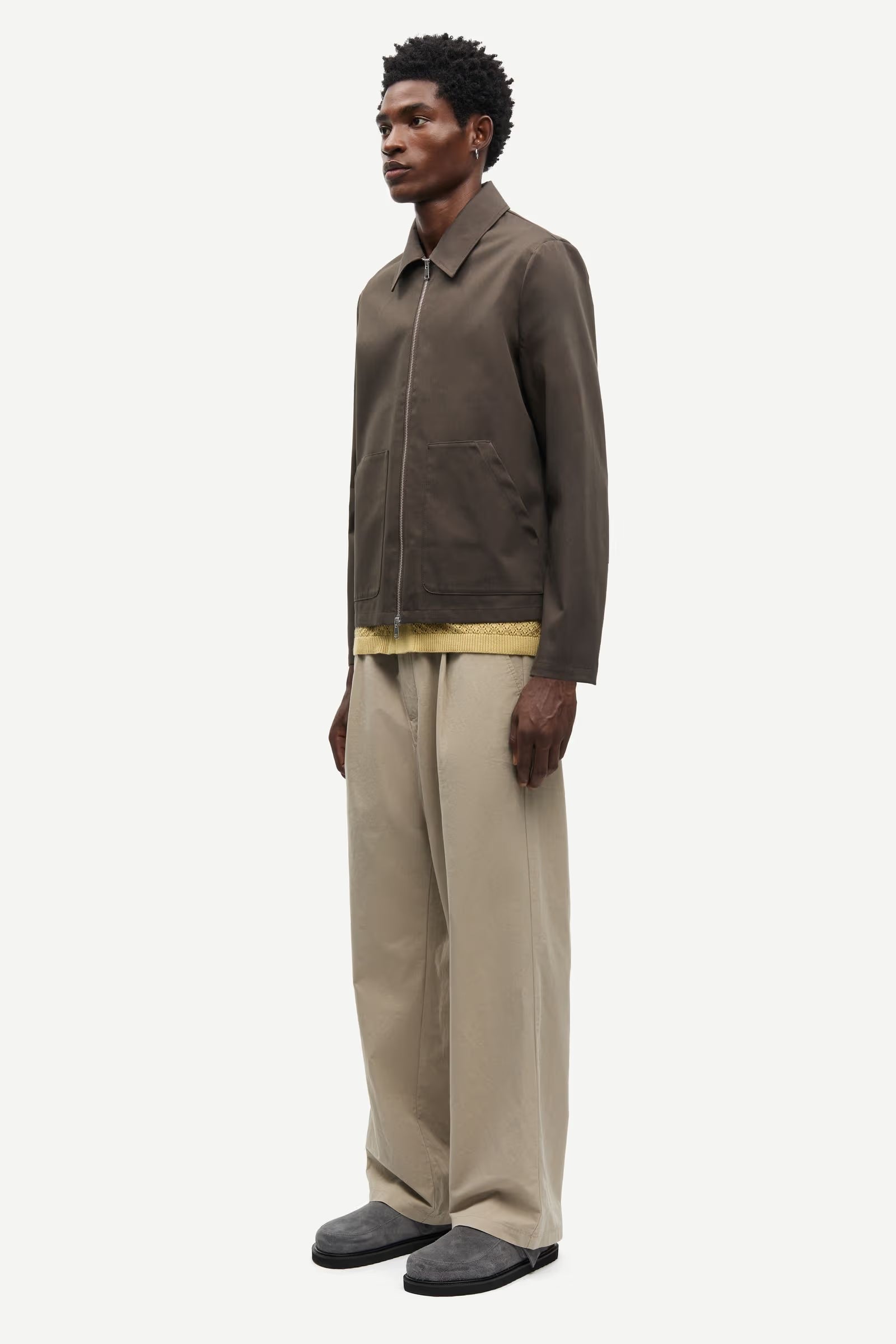 Man wearing a brown jacket by Samsoe Samsoe and beige pants on a white background side view