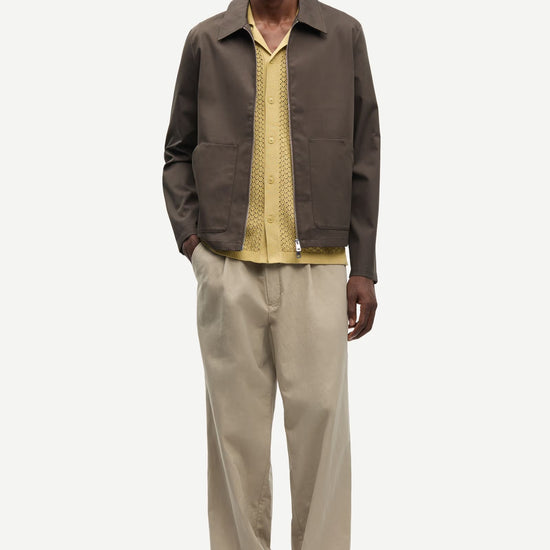 Man wearing a brown jacket by Samsoe Samsoe and beige pants on a white background front view