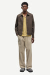 Man wearing a brown jacket by Samsoe Samsoe and beige pants on a white background front view