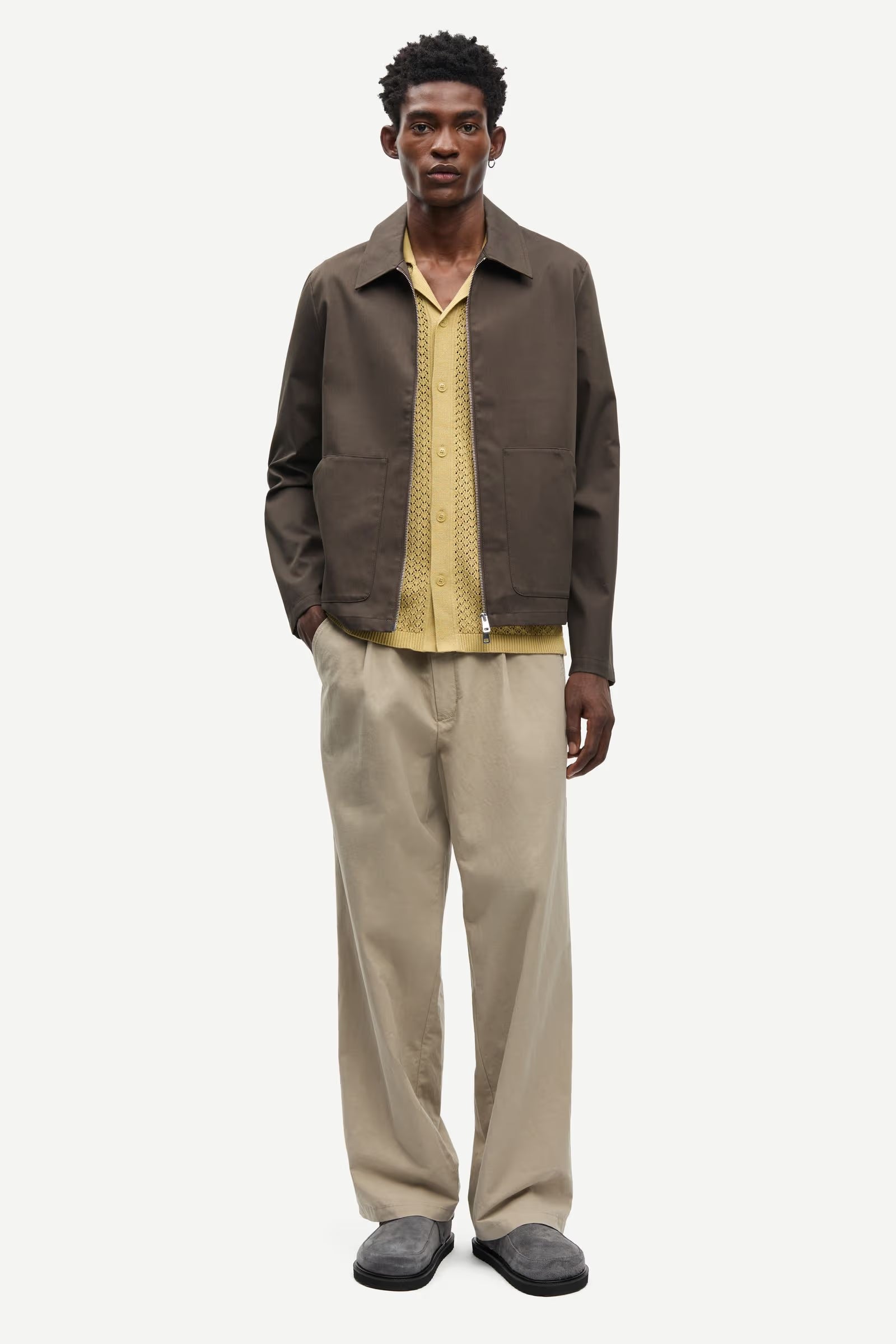 Man wearing a brown jacket by Samsoe Samsoe and beige pants on a white background front view