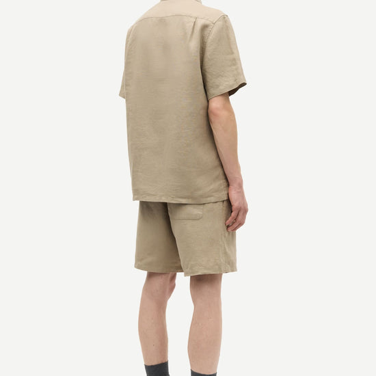 Man wearing a beige shirt and shorts set on a white background rear view