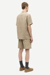 Man wearing a beige shirt and shorts set on a white background rear view