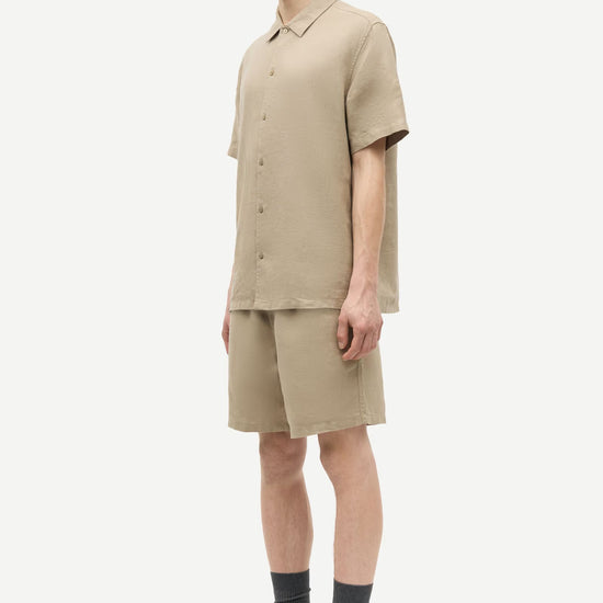 Person wearing a beige outfit with shorts and a shirt by Samsoe Samsoe on a white background side view