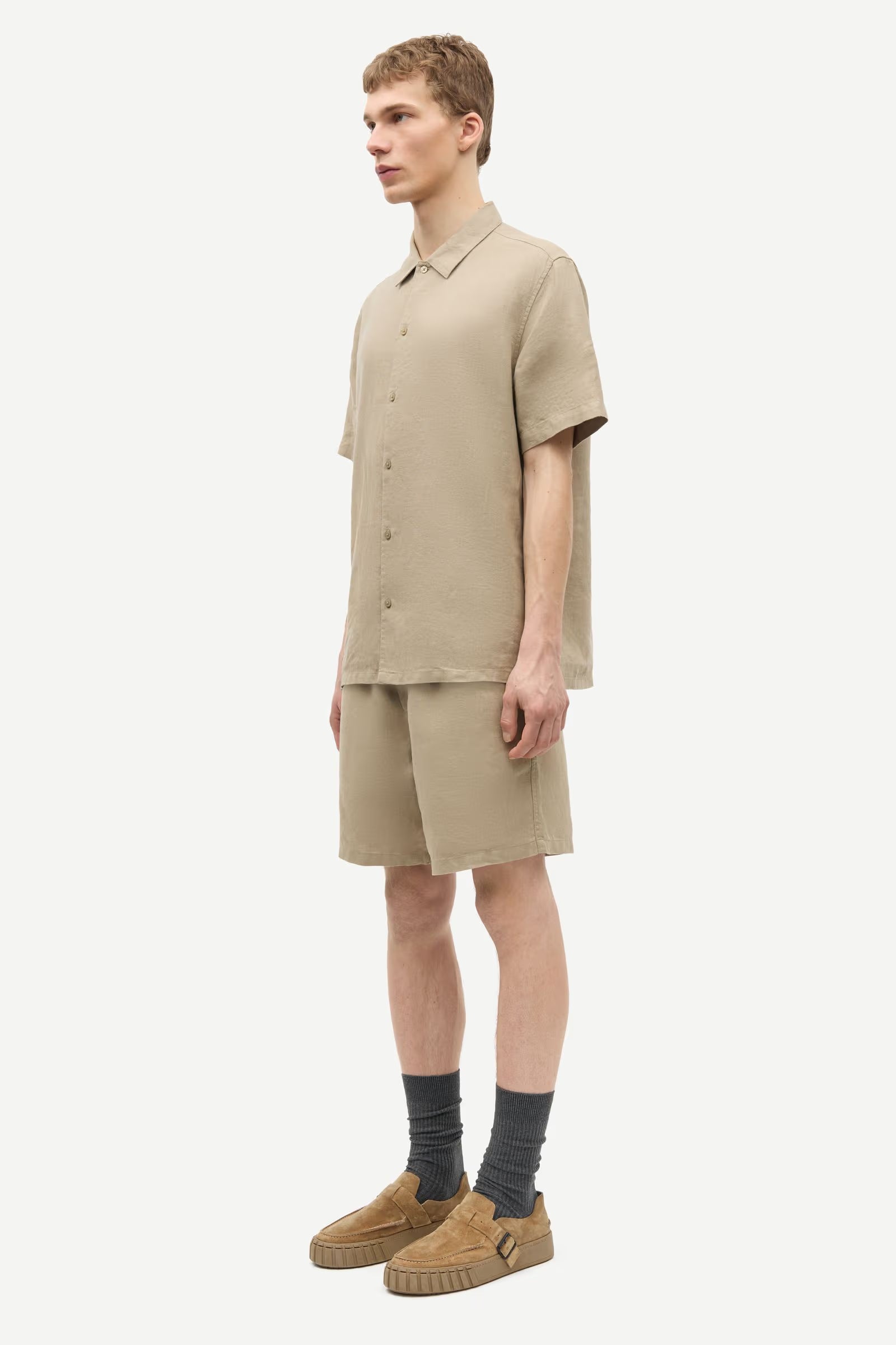 Person wearing a beige outfit with shorts and a shirt by Samsoe Samsoe on a white background side view