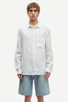 Man wearing a blue and white striped shirt by Samsoe Samsoe and denim shorts on a white background