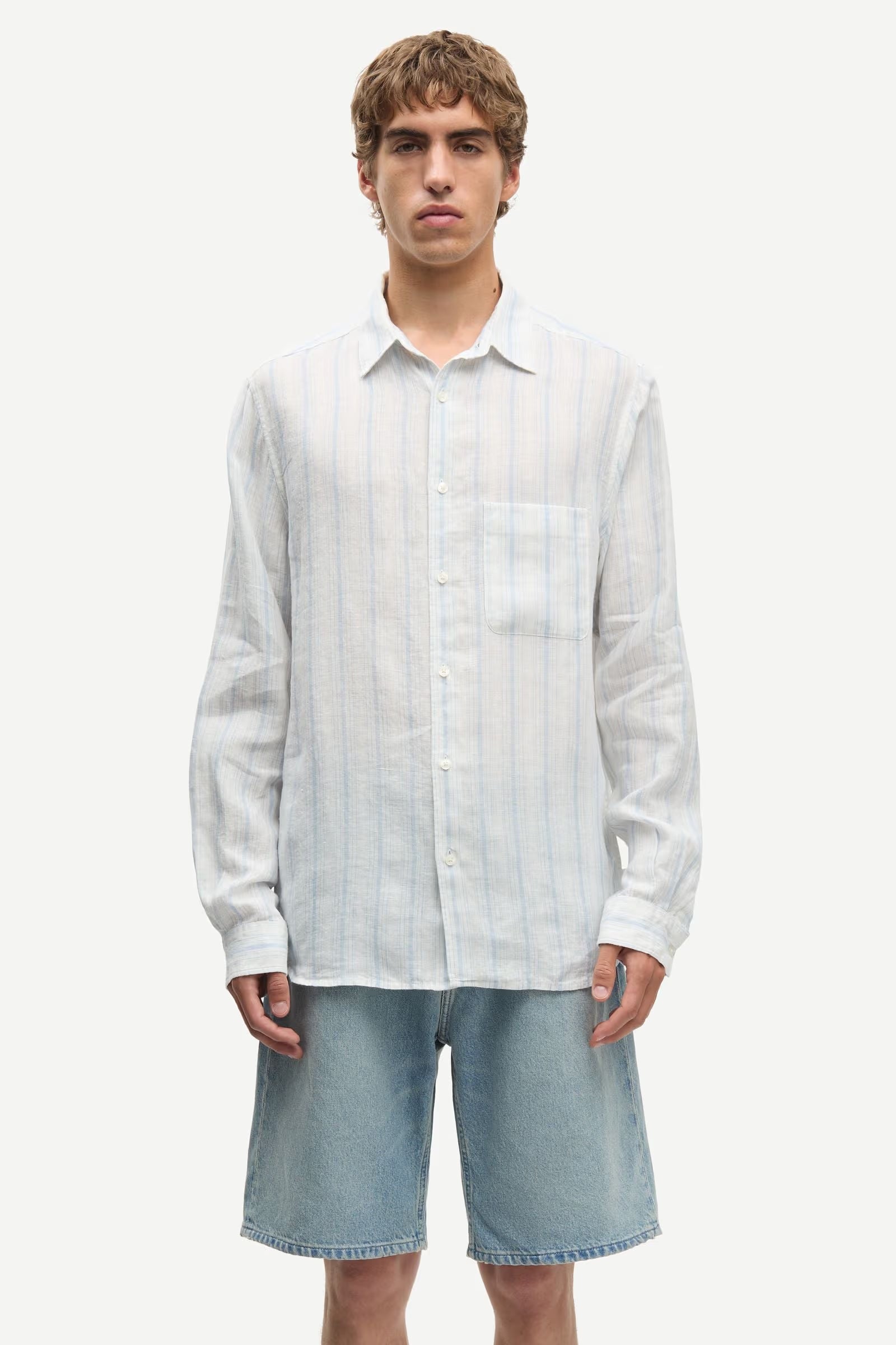 Man wearing a blue and white striped shirt by Samsoe Samsoe and denim shorts on a white background