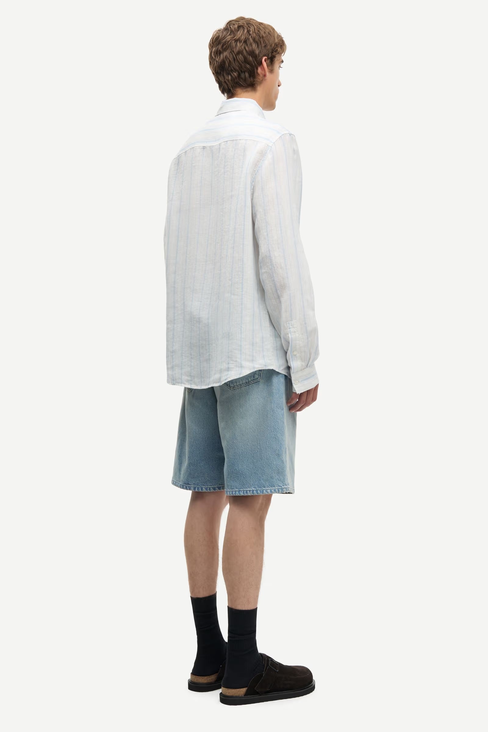 Man wearing a blue and white striped shirt by Samsoe Samsoe and denim shorts on a white background rear view