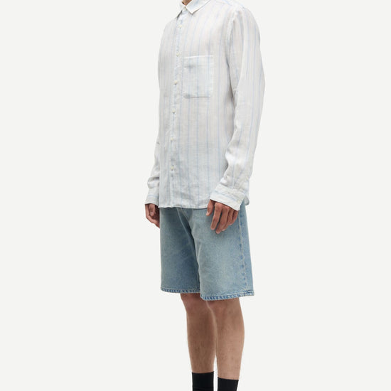 Man wearing a blue and white striped shirt by Samsoe Samsoe and denim shorts on a white background side view