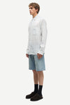 Man wearing a blue and white striped shirt by Samsoe Samsoe and denim shorts on a white background side view