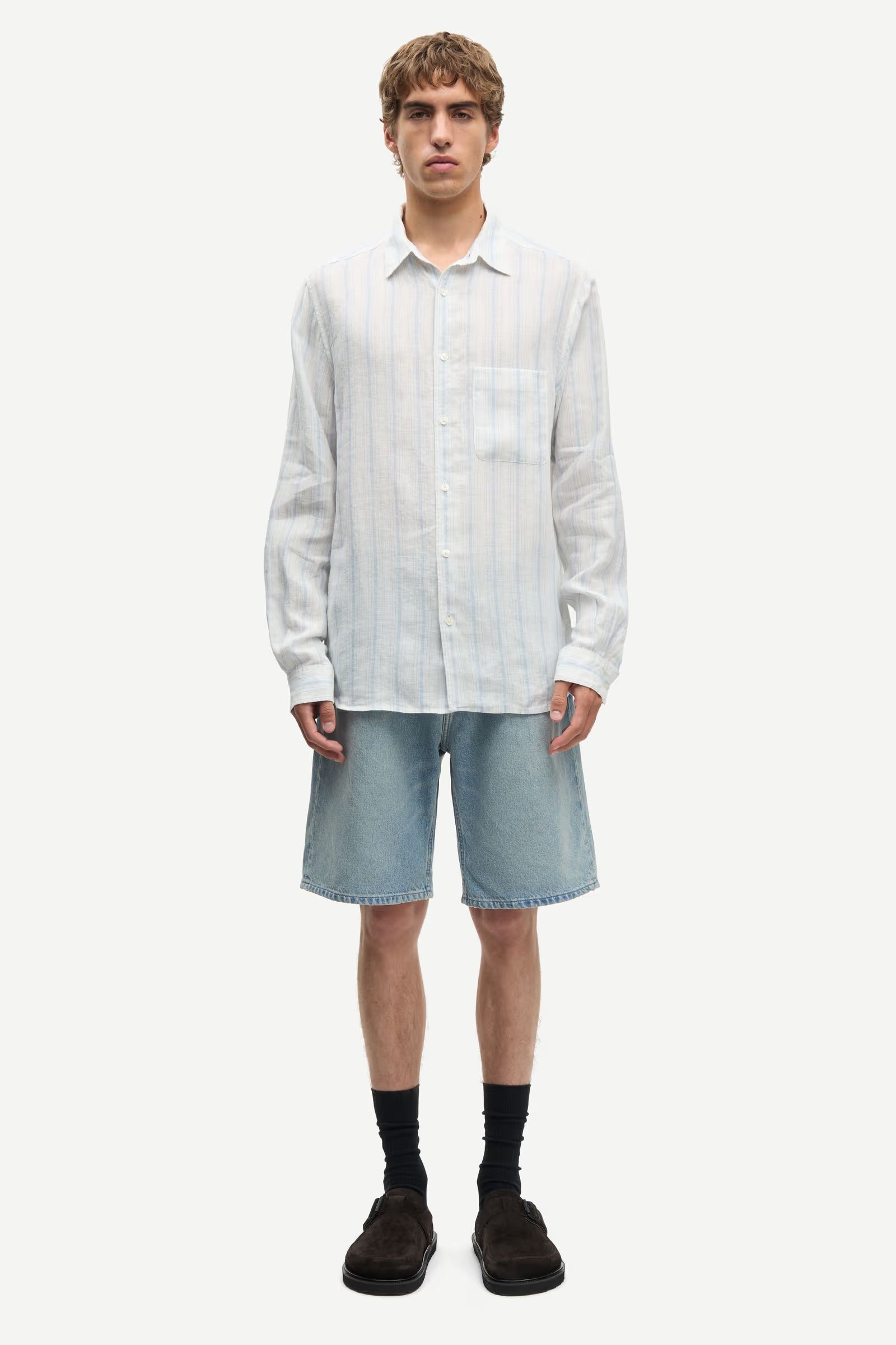 Man wearing a blue and white striped shirt by Samsoe Samsoe and denim shorts on a white background full outfit