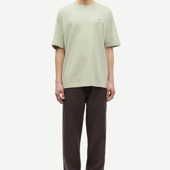 Man wearing a light green t-shirt and brown pants by Samsoe Samsoe on a white background