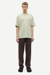Man wearing a light green t-shirt and brown pants by Samsoe Samsoe on a white background