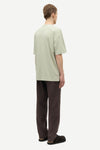 Man wearing a light green t-shirt and brown pants by Samsoe Samsoe on a white background rear view