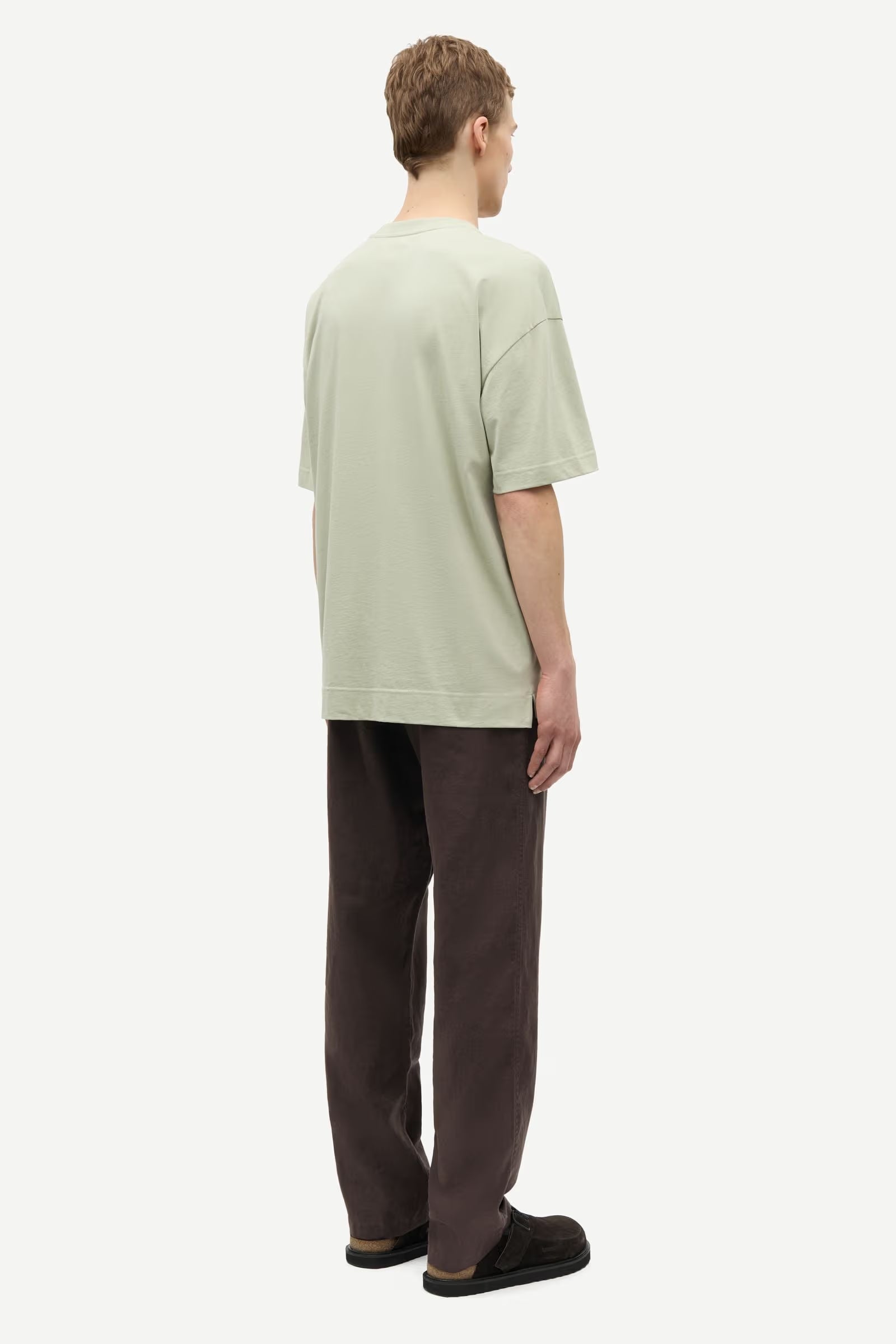 Man wearing a light green t-shirt and brown pants by Samsoe Samsoe on a white background rear view