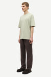 Man wearing a light green t-shirt and brown pants by Samsoe Samsoe on a white background side view