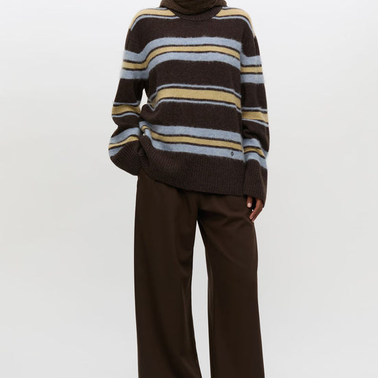 Woman wearing striped brown yellow and pale blue knit with brown trousers