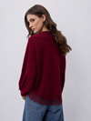 A woman wearing a deep burgundy knit sweater with a lace hem, paired with blue jeans, photographed from the back against a light gray studio background.