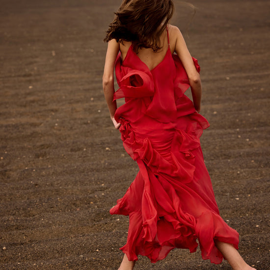 Person in a red dress walking on a dark sandy beach.