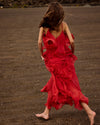 Person in a red dress walking on a dark sandy beach.