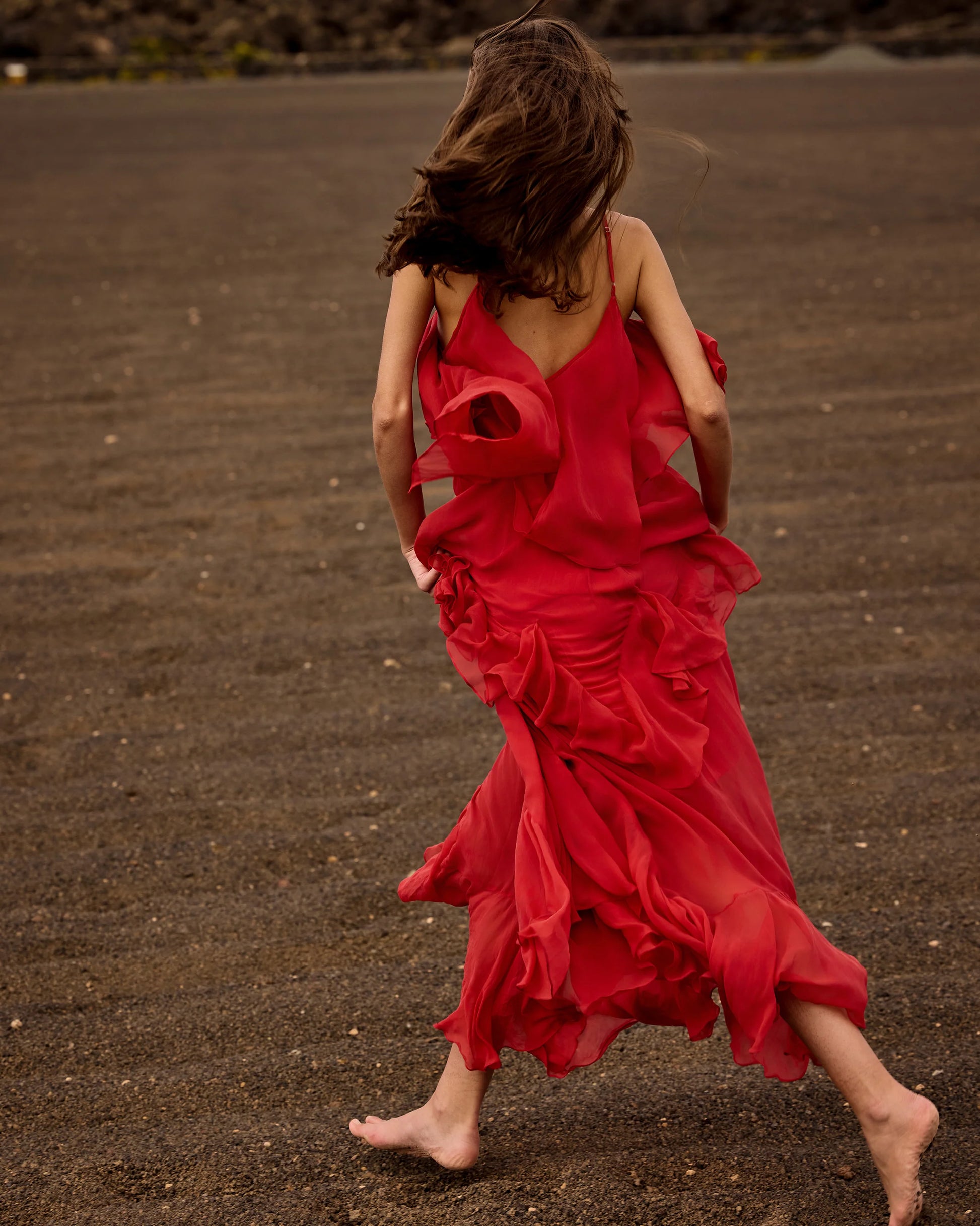 Person in a red dress walking on a dark sandy beach.