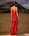 Woman in a red dress standing in a desert landscape with mountains in the background rear view