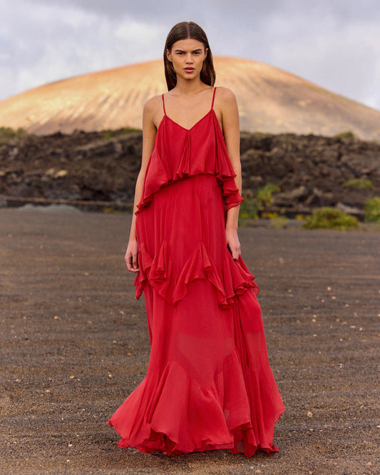 Woman in a red dress standing in a desert-like landscape with mountains in the background