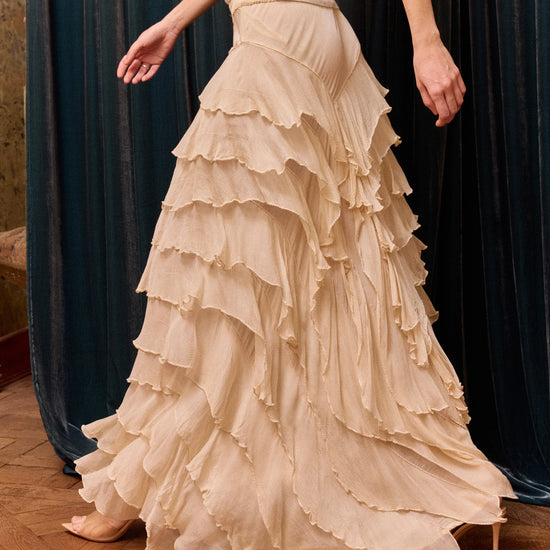 Beige ruffled skirt worn by a person on a wooden floor with dark curtains in the background
