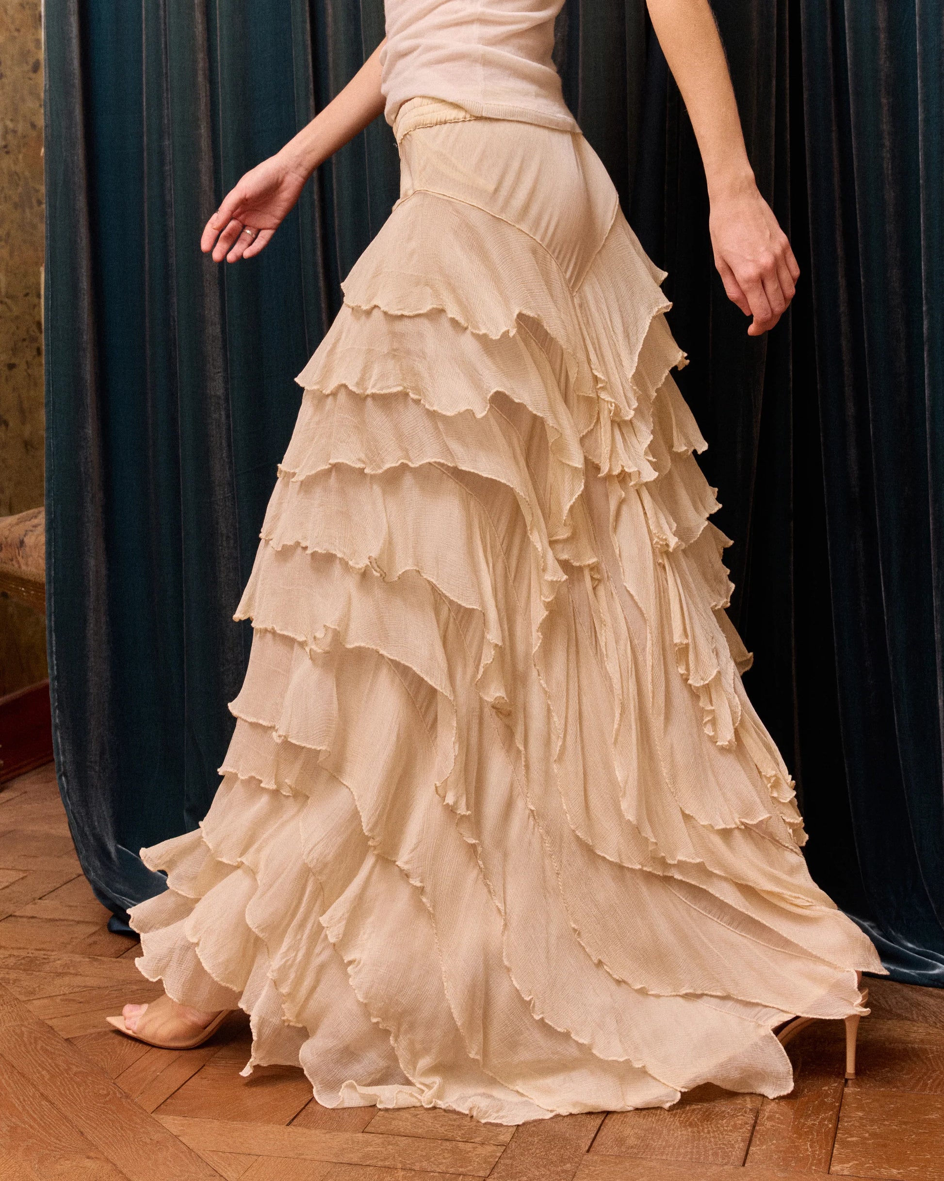 Beige ruffled skirt worn by a person on a wooden floor with dark curtains in the background