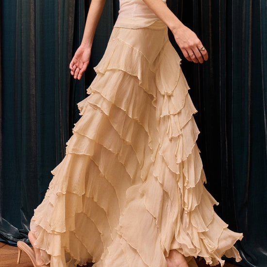 Woman wearing a beige ruffled dress against a dark curtain background