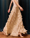 Woman wearing a beige ruffled dress against a dark curtain background