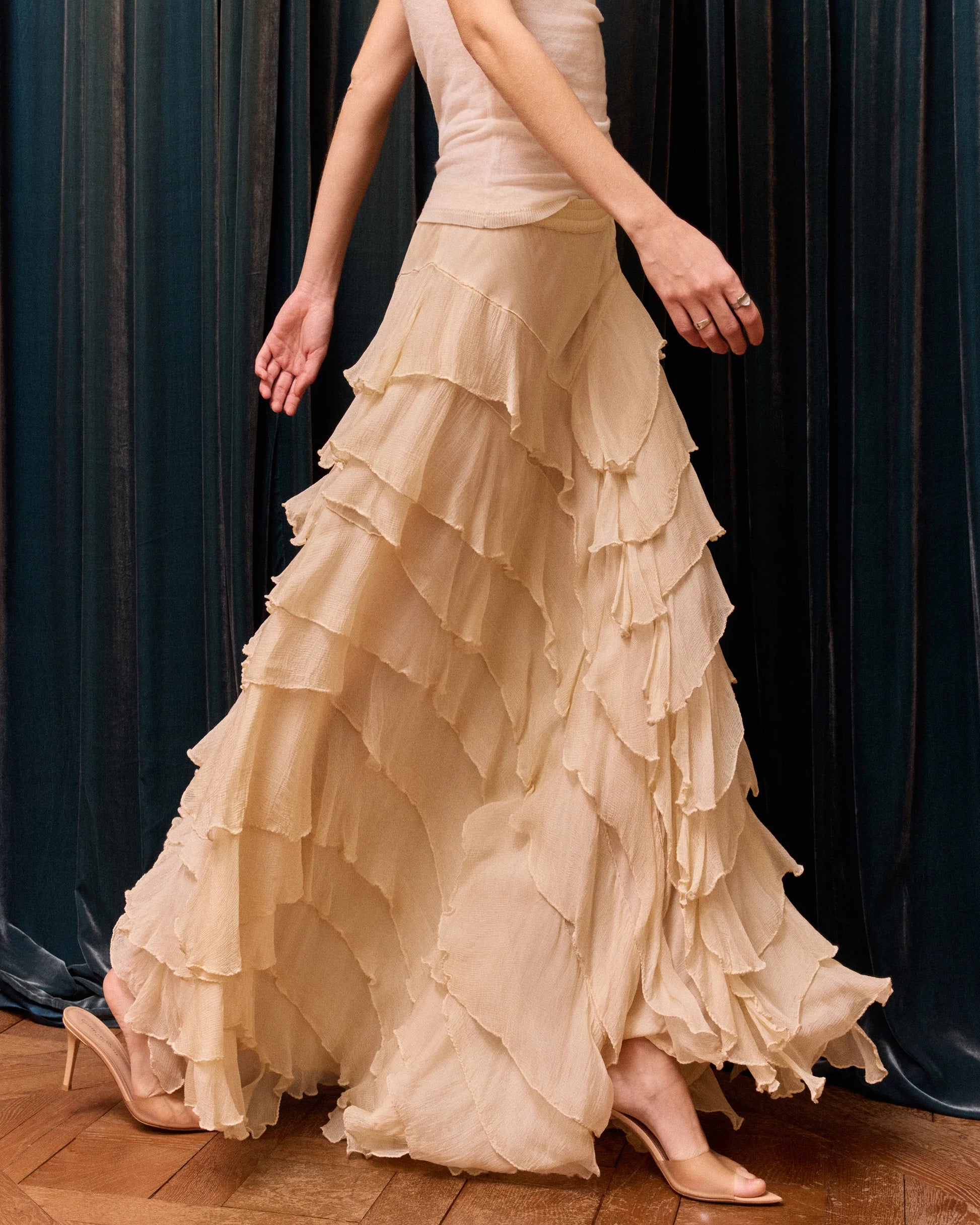 Woman wearing a beige ruffled dress against a dark curtain background