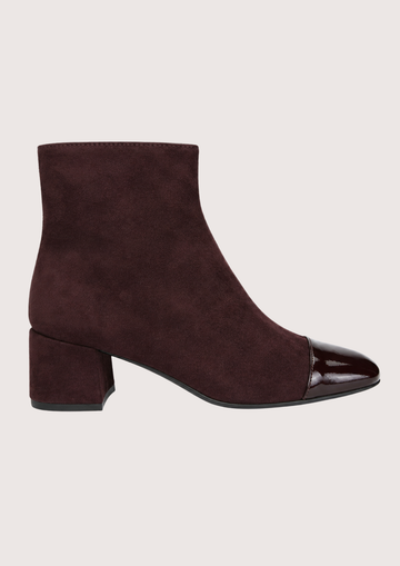 A dark burgundy suede ankle boot with a glossy patent leather cap toe and a low block heel, shown in profile against a light beige background.